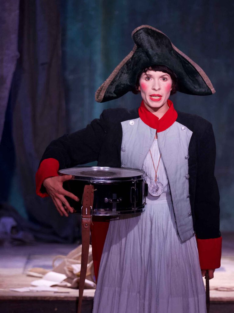 Elisabeth Taraba spielt einen hessischen Söldner im amerikanischen Unabhängigkeitskrieg aus dem Theaterstück "Sterntaler" mit Soldatenrock, Trommel, und Dreispitz. (Märchenhütten)